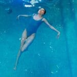 Kobieta w niebieskim stroju kąpielowym unosi się na wodzie w basenie