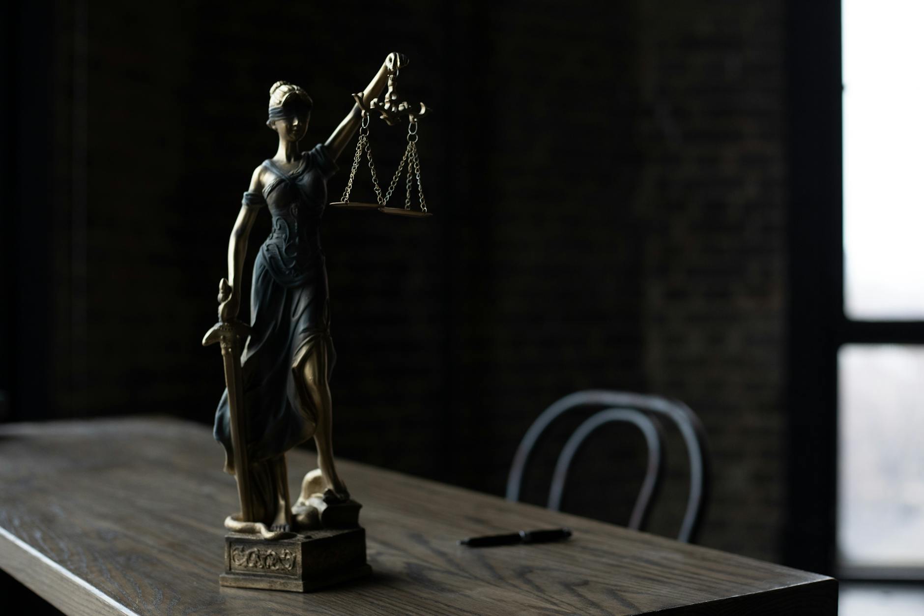Figurka Temidy na drewnianym stole w przyciemnionym pokoju