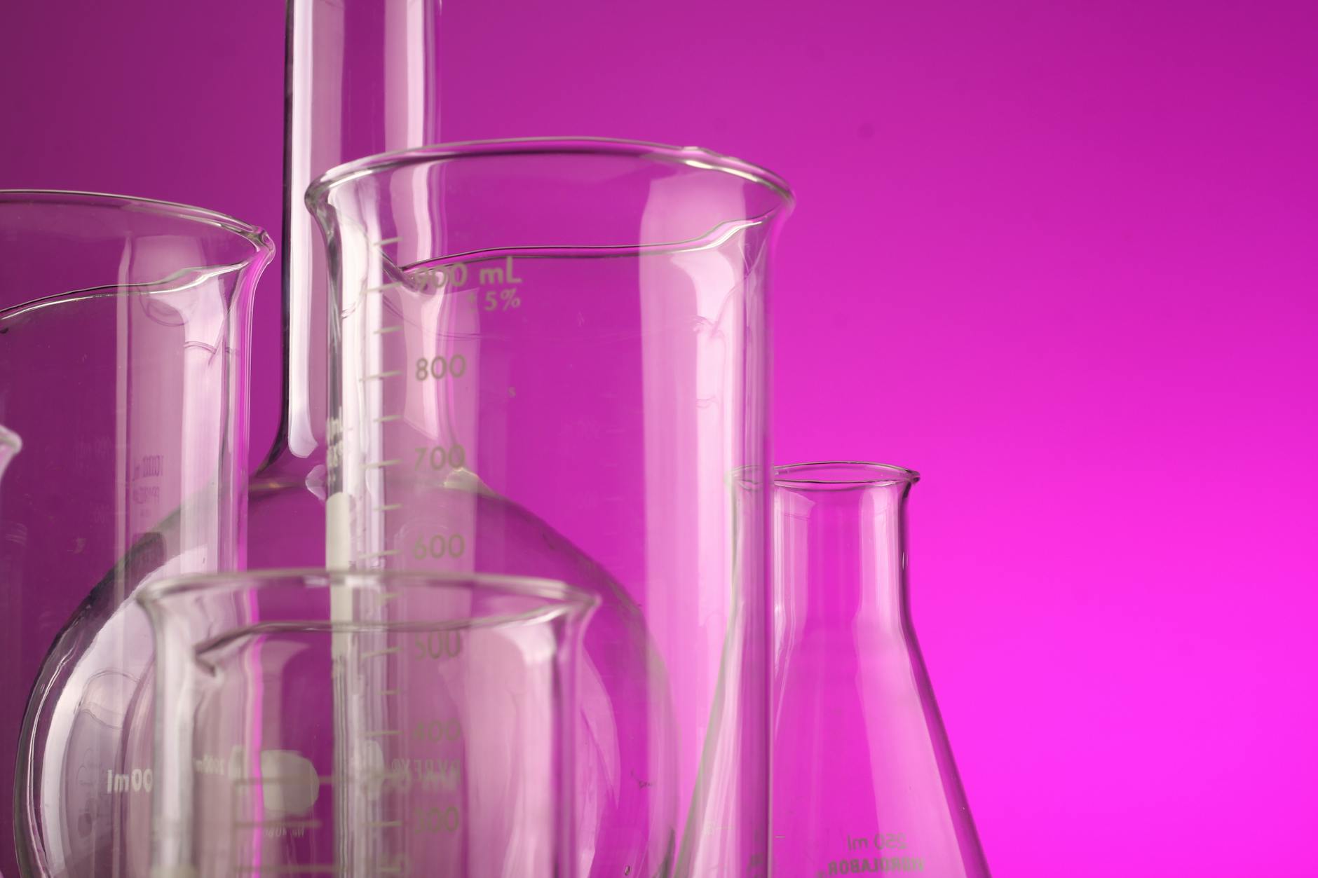 Kolby miarowe z przezroczystego szkła na fioletowym tle laboratoryjnym