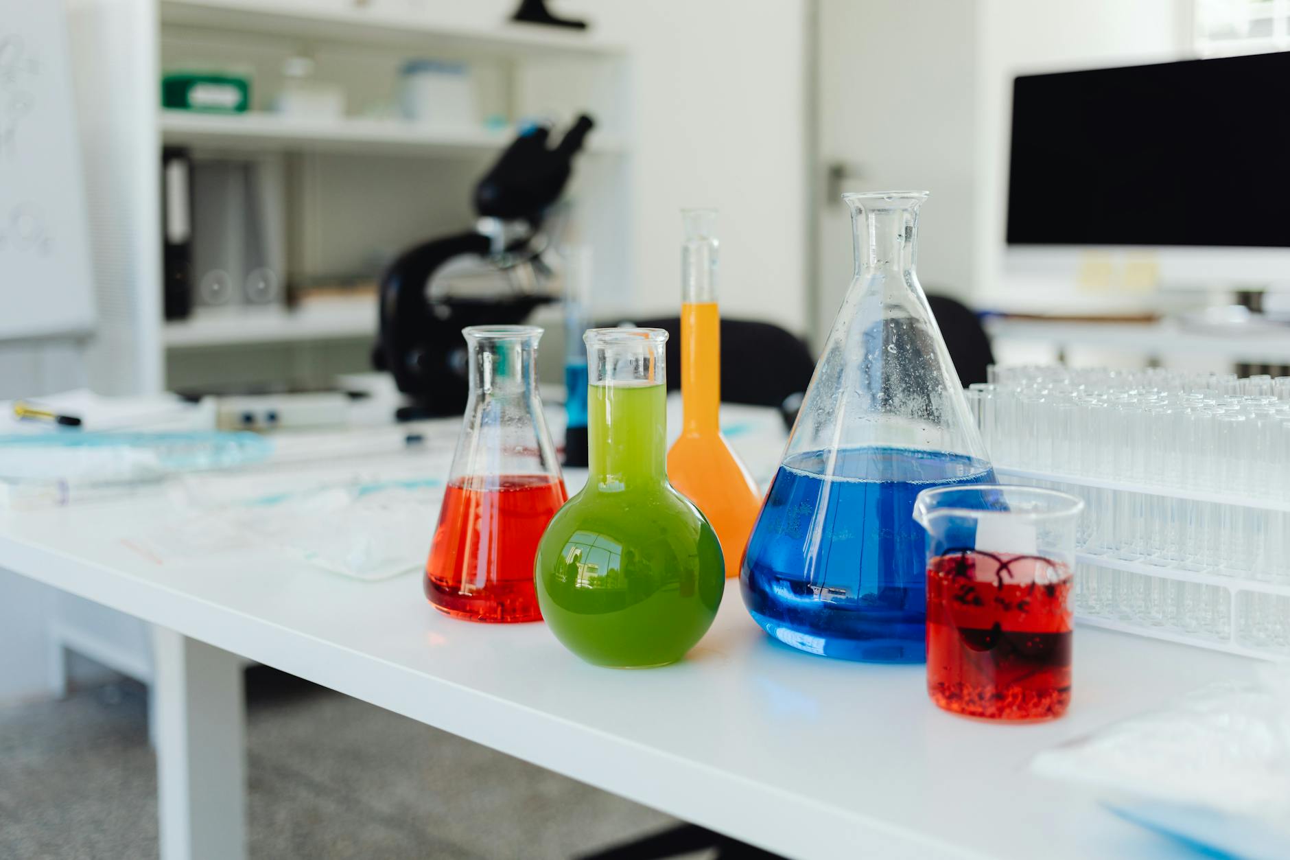 Kolorowe odczynniki chemiczne w kolbach i zlewkach na stole laboratoryjnym