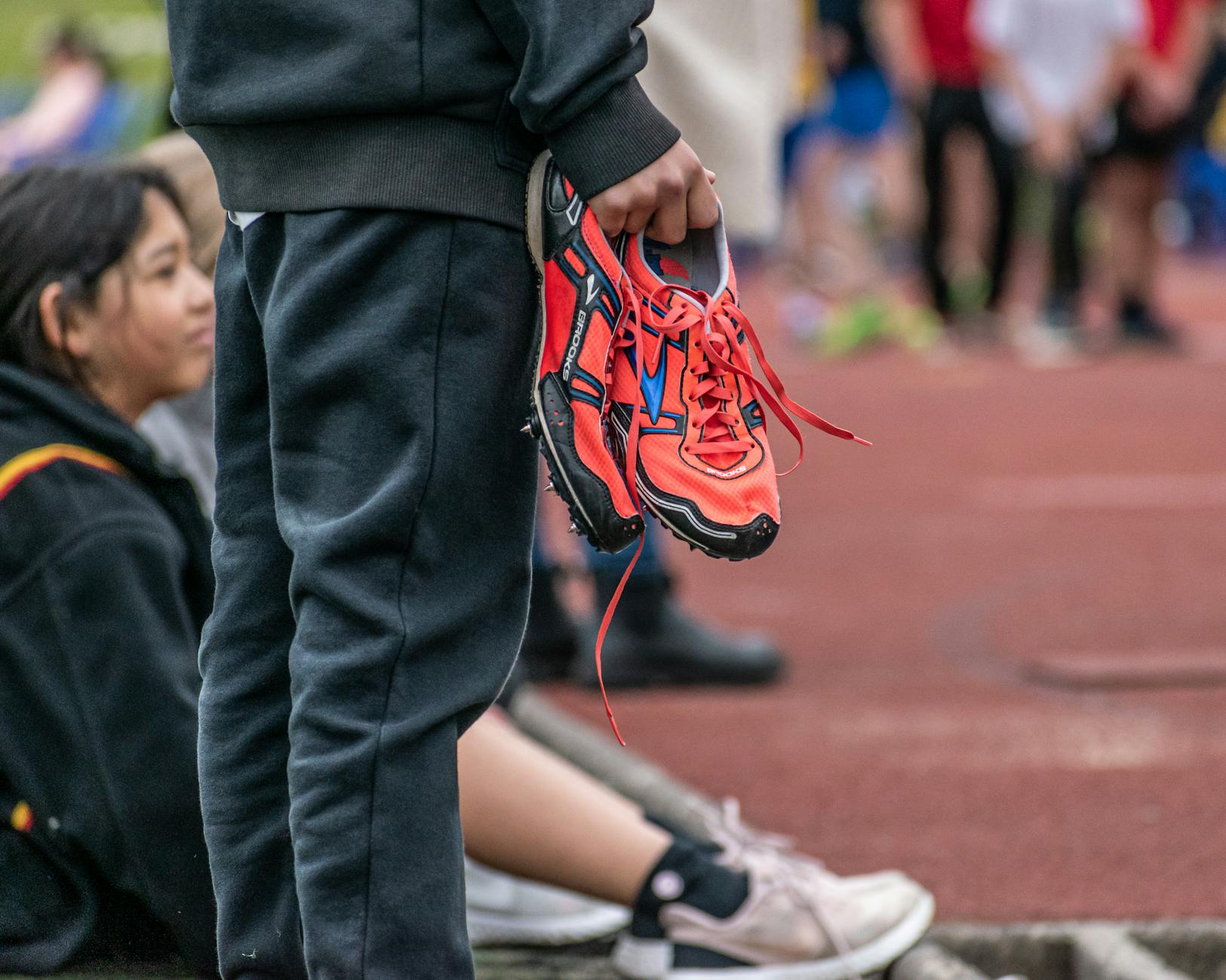 Uczeń trzyma czerwone buty biegowe przy szkolnej bieżni
