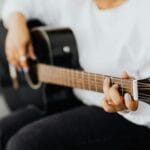 Dłoń początkującego gitarzysty ustawiająca akord na gryfie gitary akustycznej