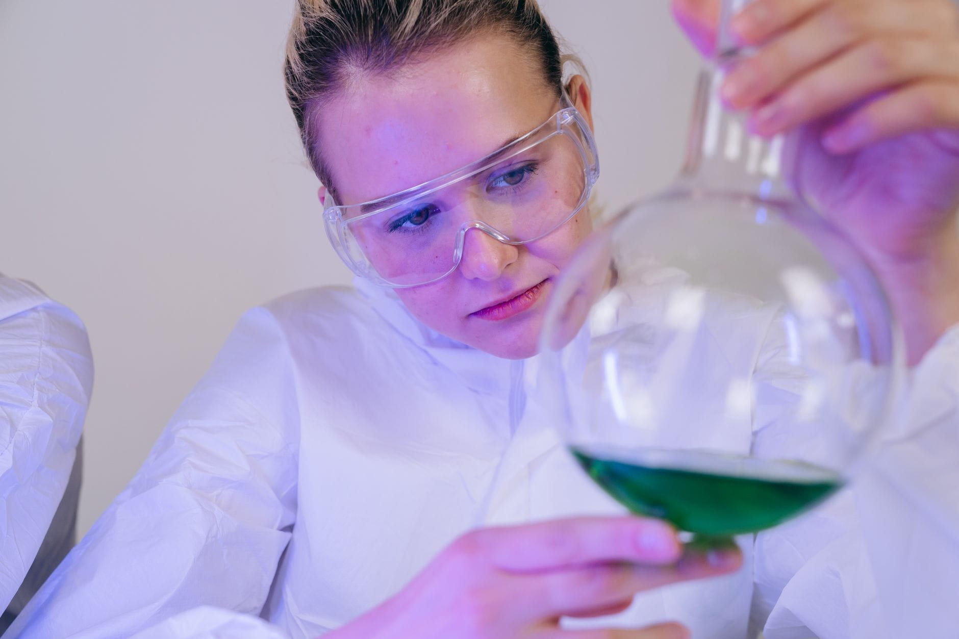 Naukowczyni bada zielony roztwór w laboratorium w okularach ochronnych