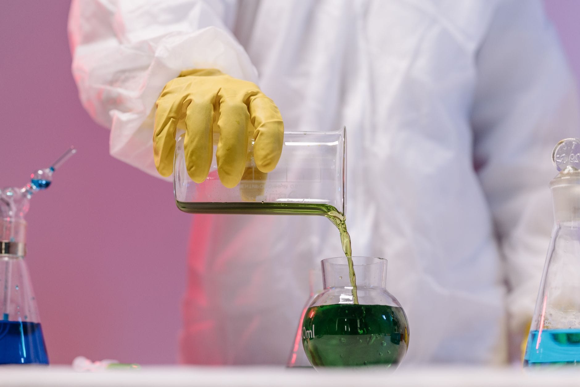 Naukowiec w odzieży ochronnej przelewa zielony płyn w laboratorium